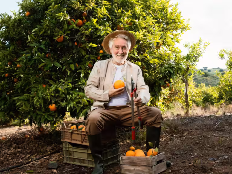Portrait de l'un des maraichers producteurs du restaurant Le Jardin des Saveurs, assis dans son verger avec des caisses d'oranges